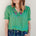 A woman wearing a green blouse with short blouson sleeves, a frill collar, and colorful parrot embroidery