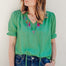 A woman wearing a green blouse with short blouson sleeves, a frill collar, and colorful parrot embroidery