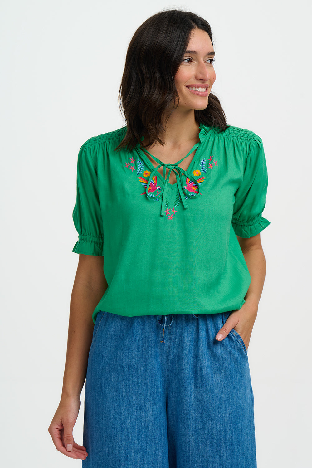Woman wearing a green blouse with floral embroidery and blue pants on a white background