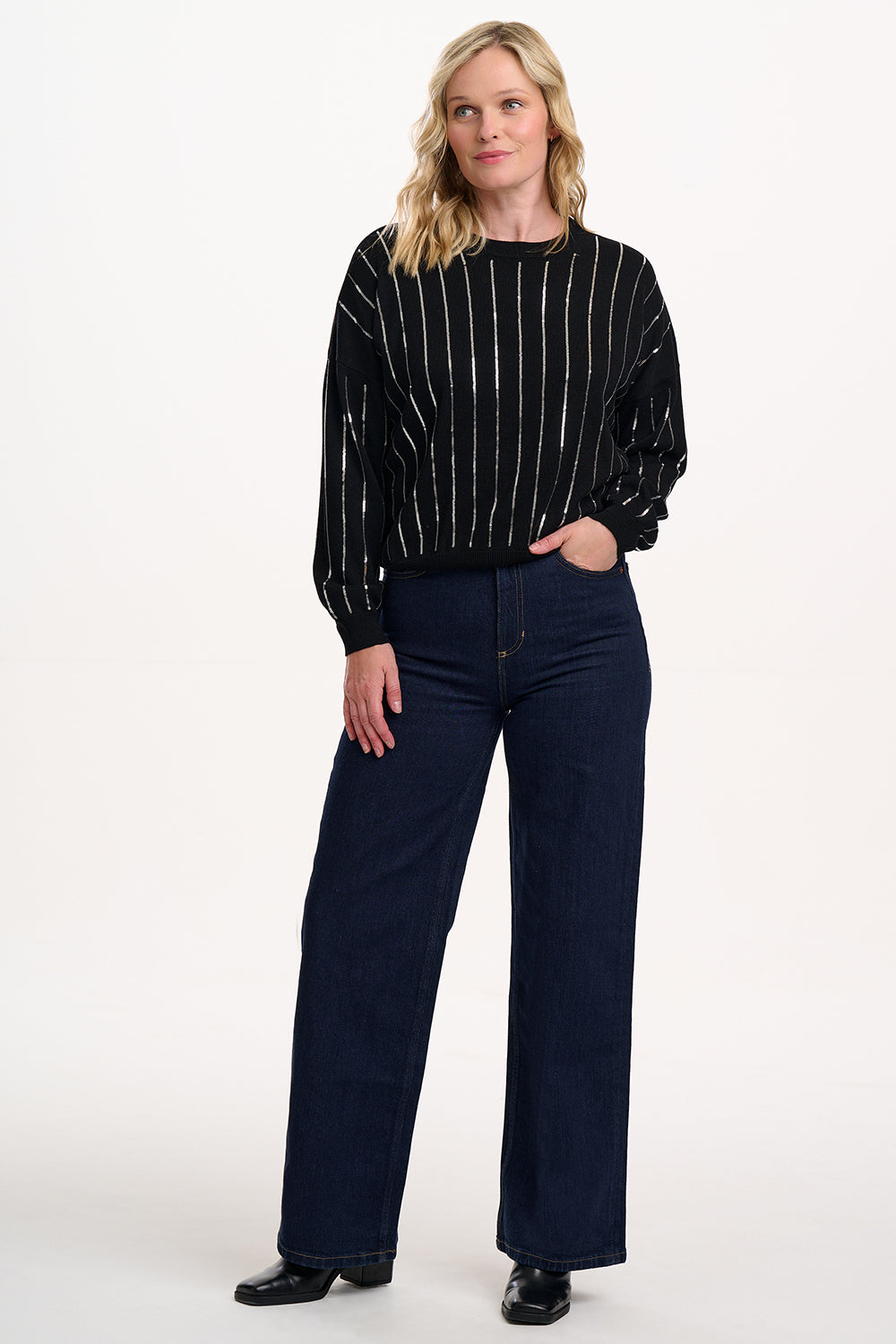 Woman wearing a black pinstripe sweater and dark blue jeans on a white background