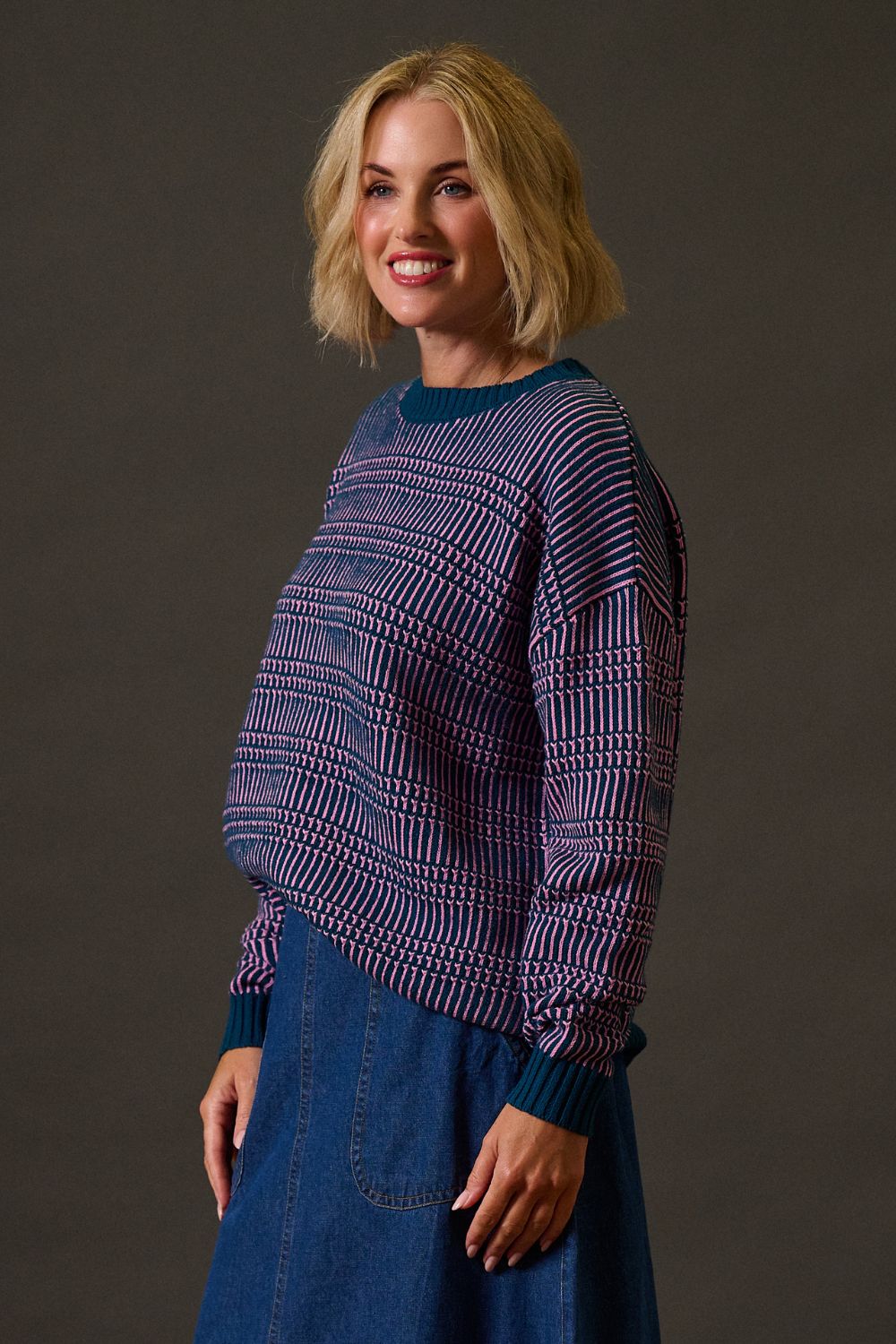 Woman wearing a patterned sweater and blue skirt against a dark background