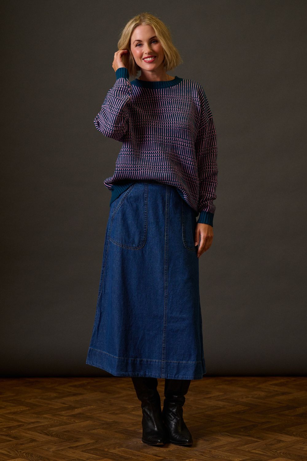 Woman wearing a purple sweater and blue denim skirt against a dark background