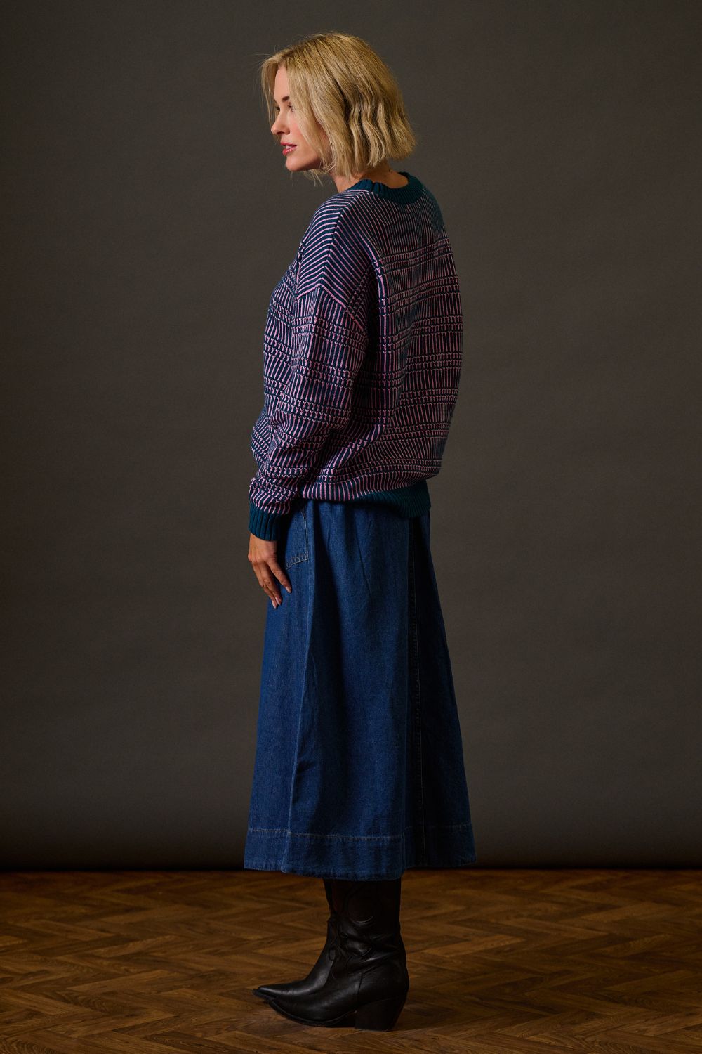 Woman wearing a patterned sweater and blue skirt against a plain background