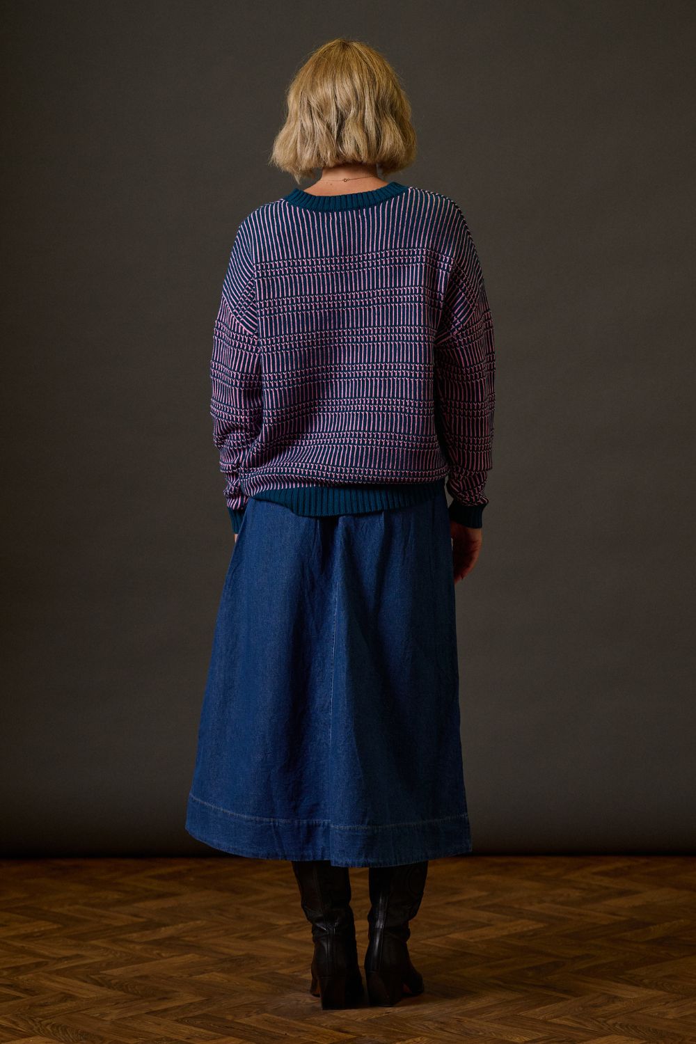 Person wearing a patterned sweater and blue skirt standing against a plain background