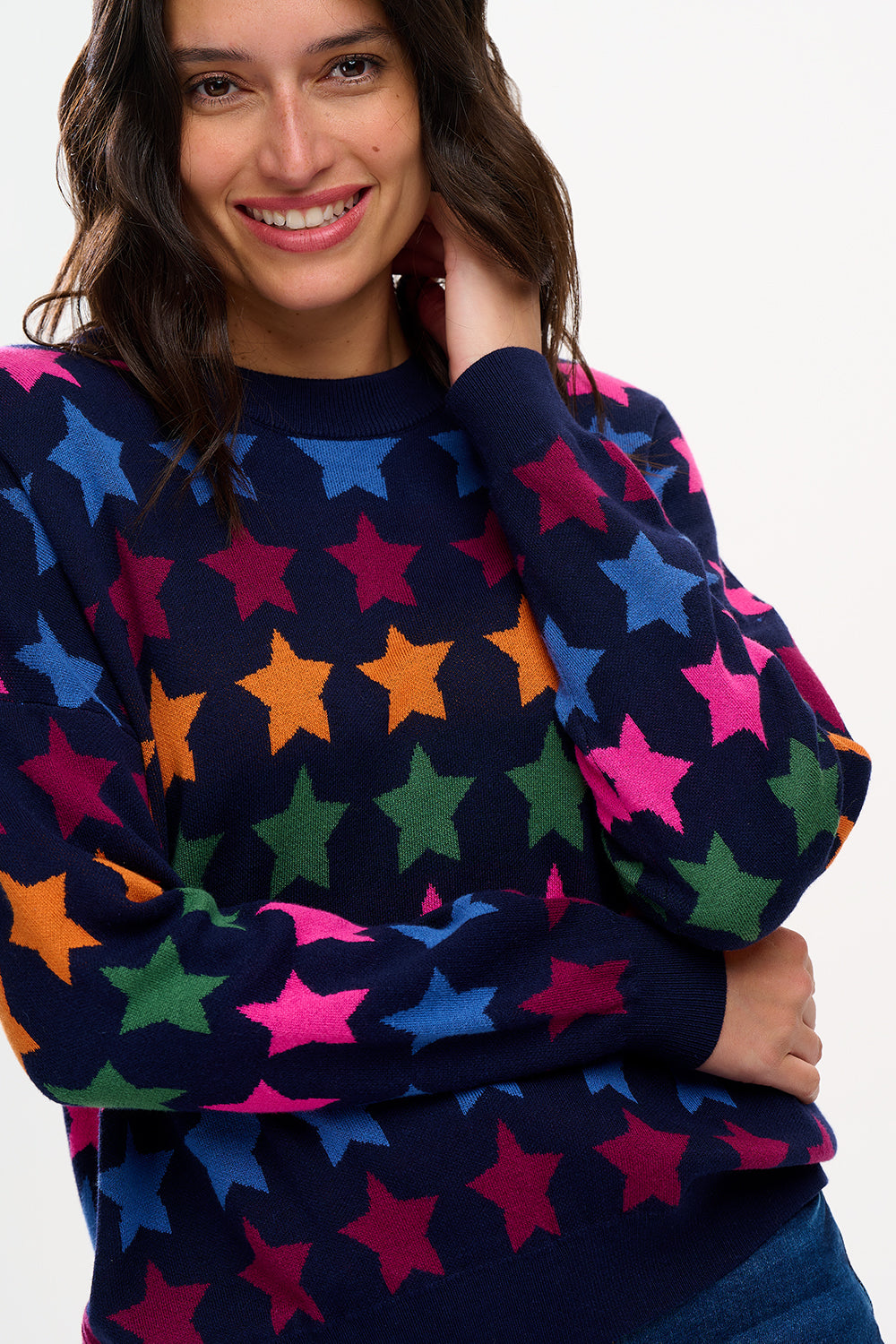 A woman smiling while wearing a multicolored star-patterned jumper with a round neckline and long sleeves.