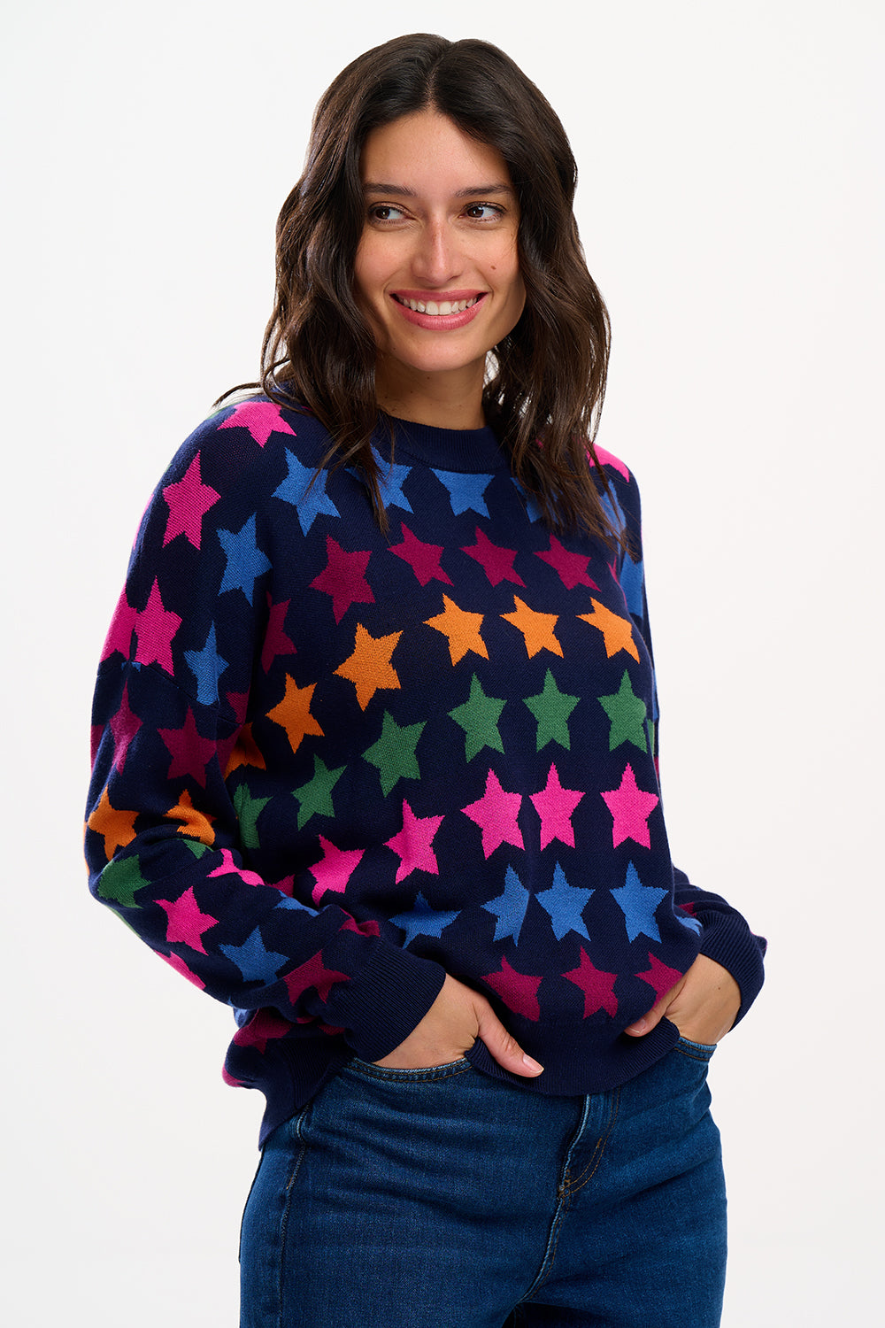 A woman smiling while wearing a multicolored star-patterned jumper with a round neckline and long sleeves.