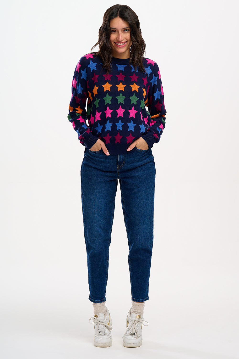 A woman smiling while wearing a multicolored star-patterned jumper with a round neckline and long sleeves.