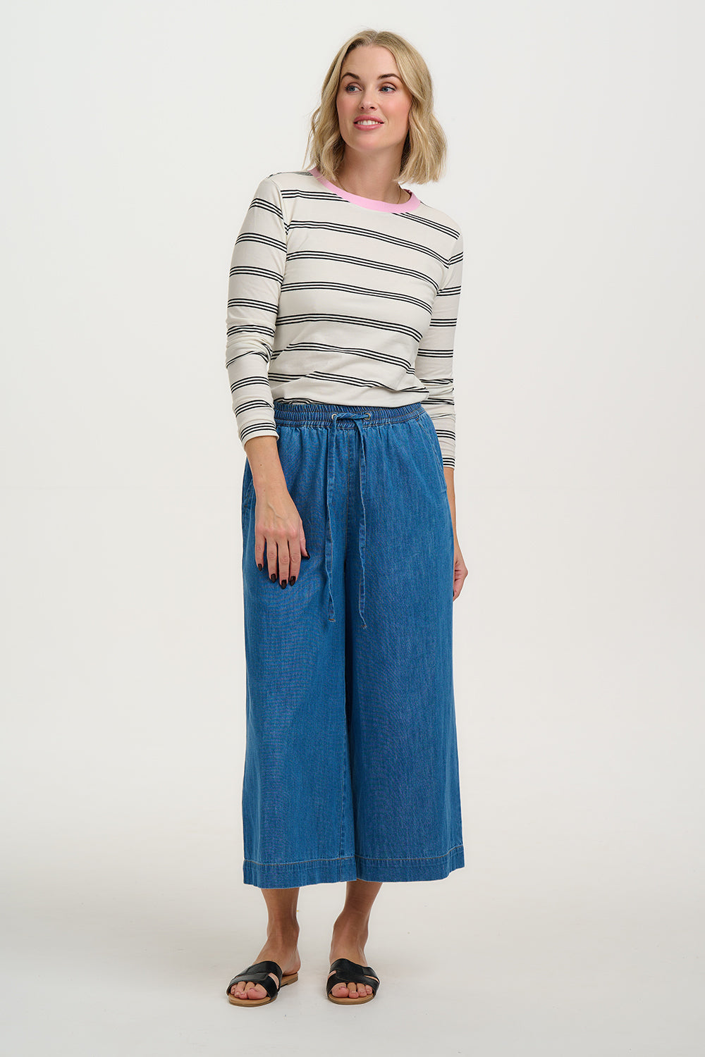 Woman wearing a striped sweater and blue wide-leg pants on a white background