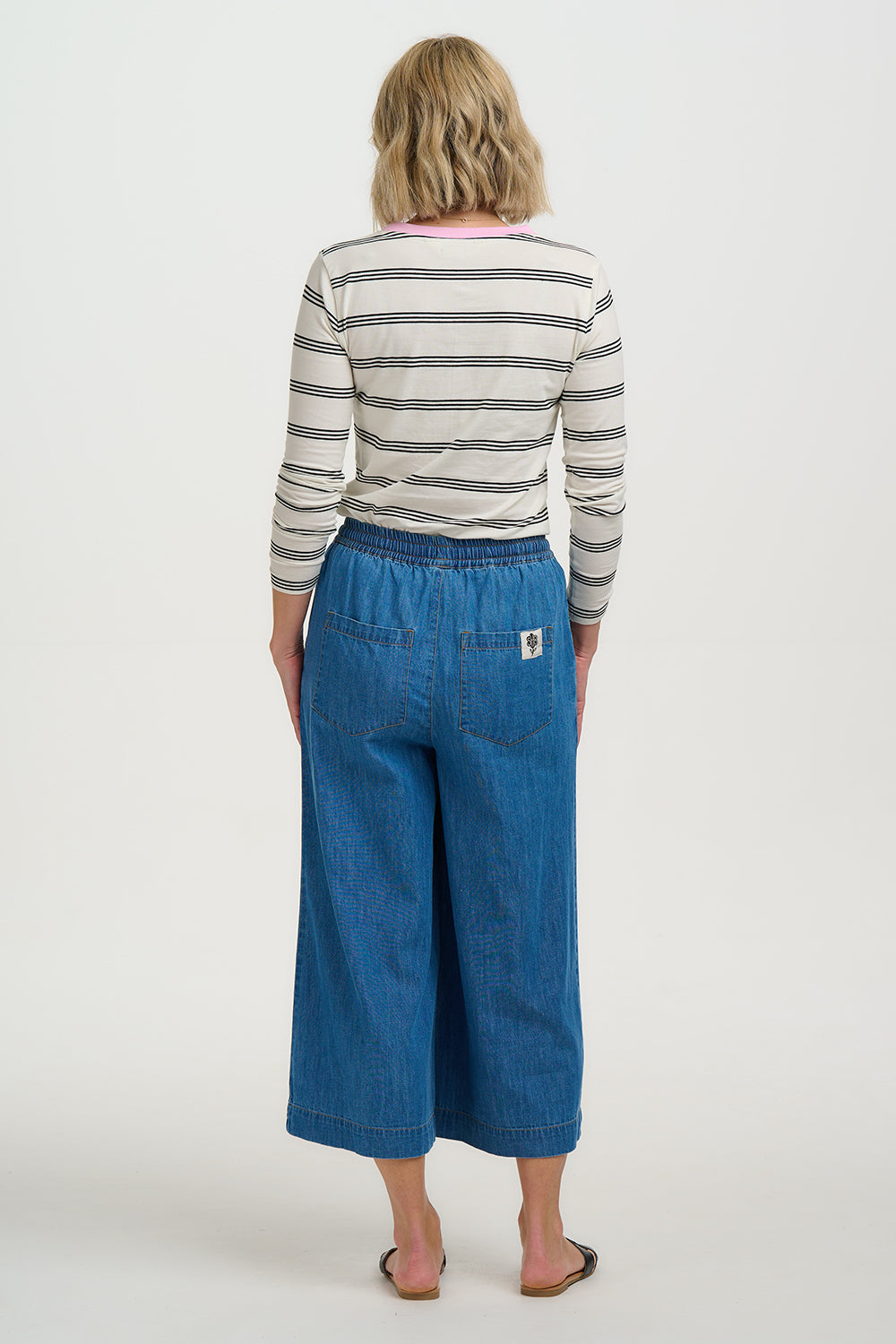 Person wearing a striped shirt and blue wide-leg pants on a white background