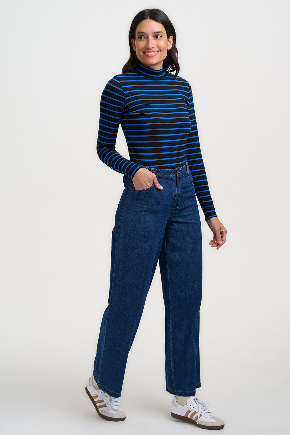 Woman wearing a blue and black striped turtleneck and blue jeans on a white background