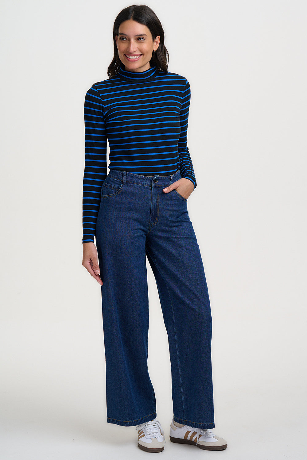 Woman wearing a blue and black striped turtleneck and wide-leg jeans on a white background