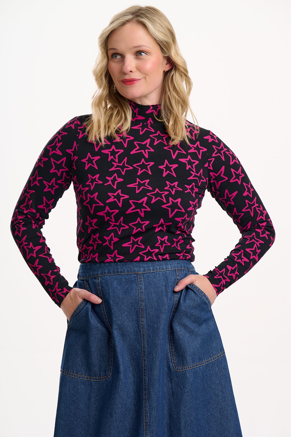 Woman wearing a black turtleneck with pink star pattern and blue jeans on a white background