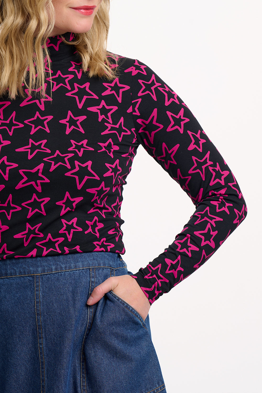 Person wearing a black long-sleeve top with pink star pattern and blue jeans on a white background