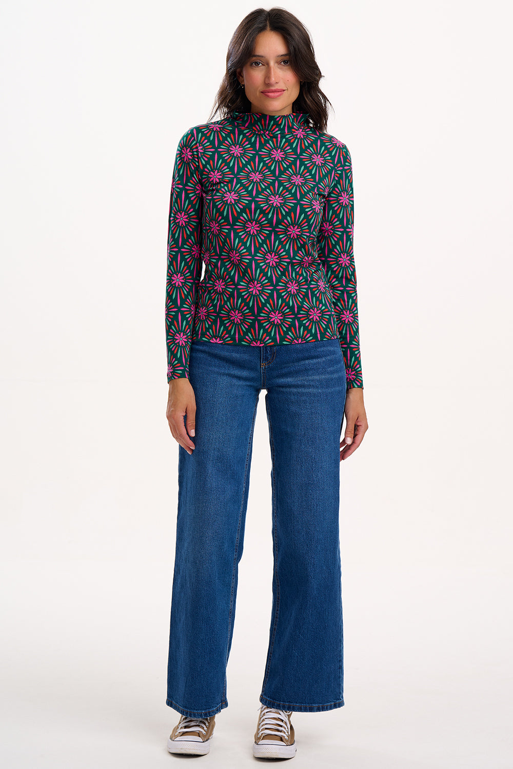 Woman wearing a patterned top and blue jeans on a white background