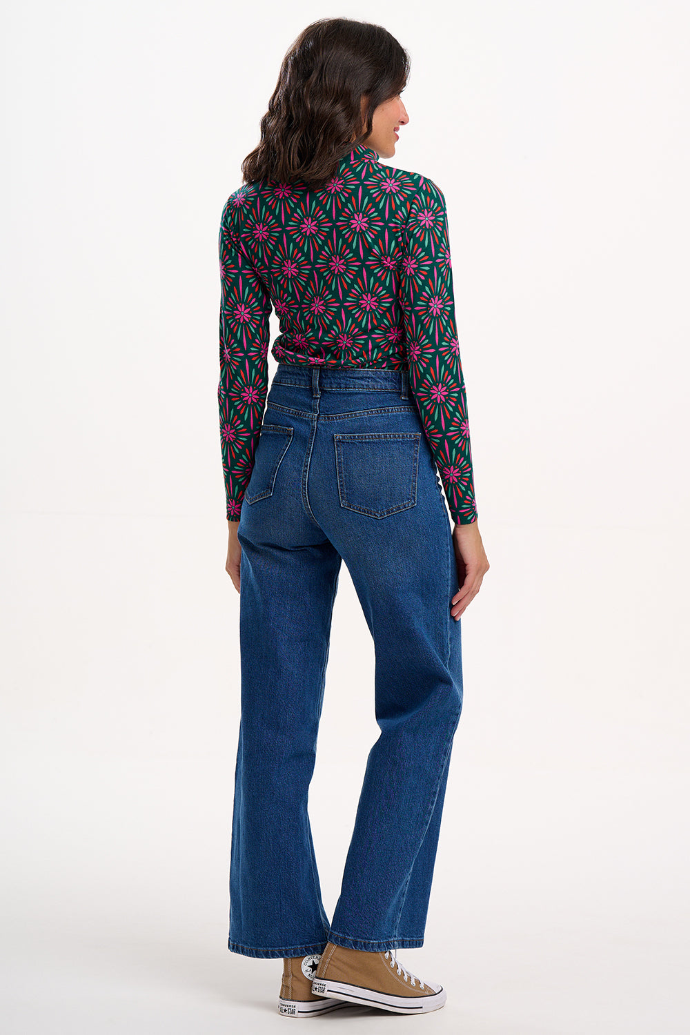 Woman wearing a patterned shirt and blue jeans on a white background