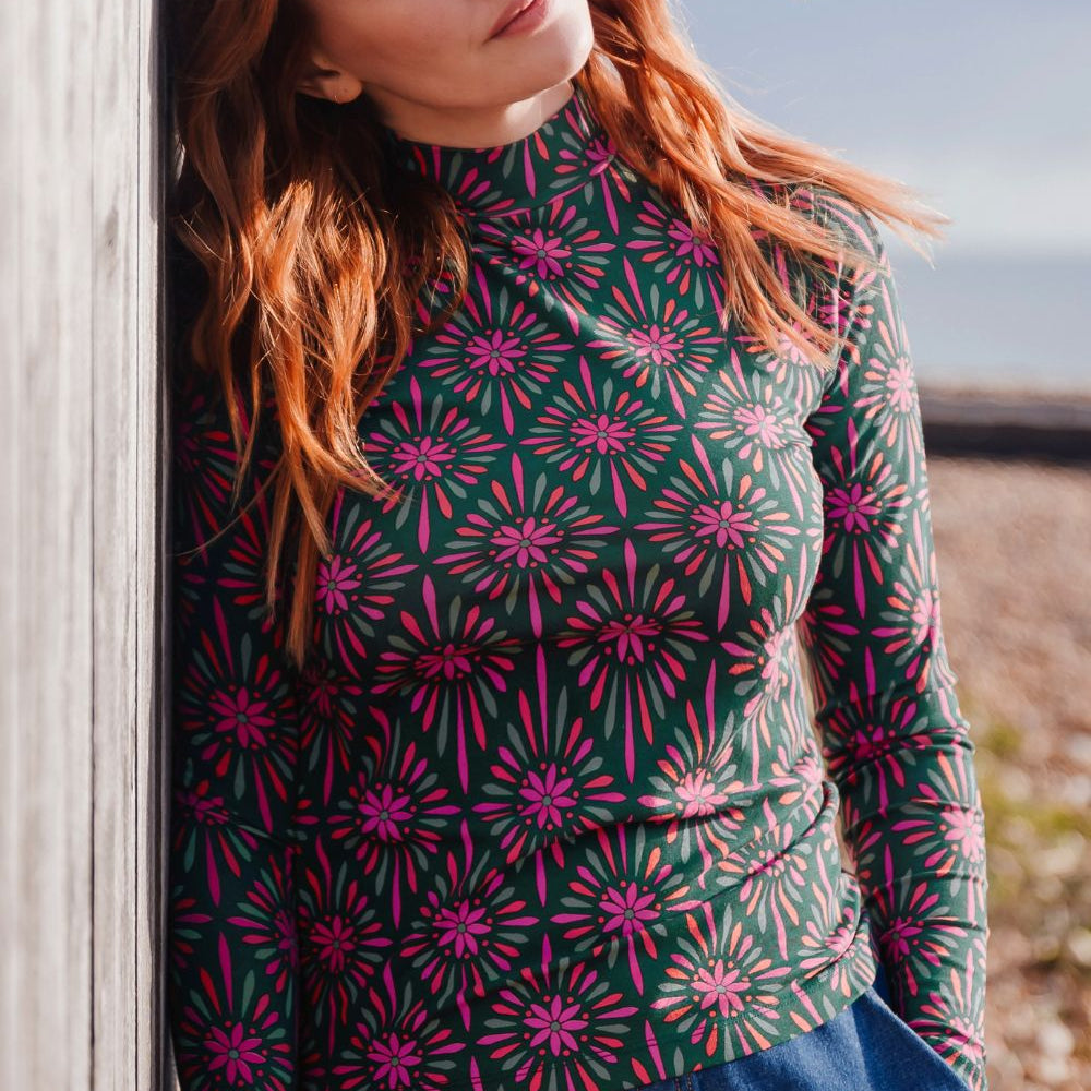 Woman wearing a patterned long-sleeve shirt leaning against a wooden post outdoors.