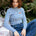 Woman wearing a blue and white striped shirt with a small red flower design, sitting outdoors.