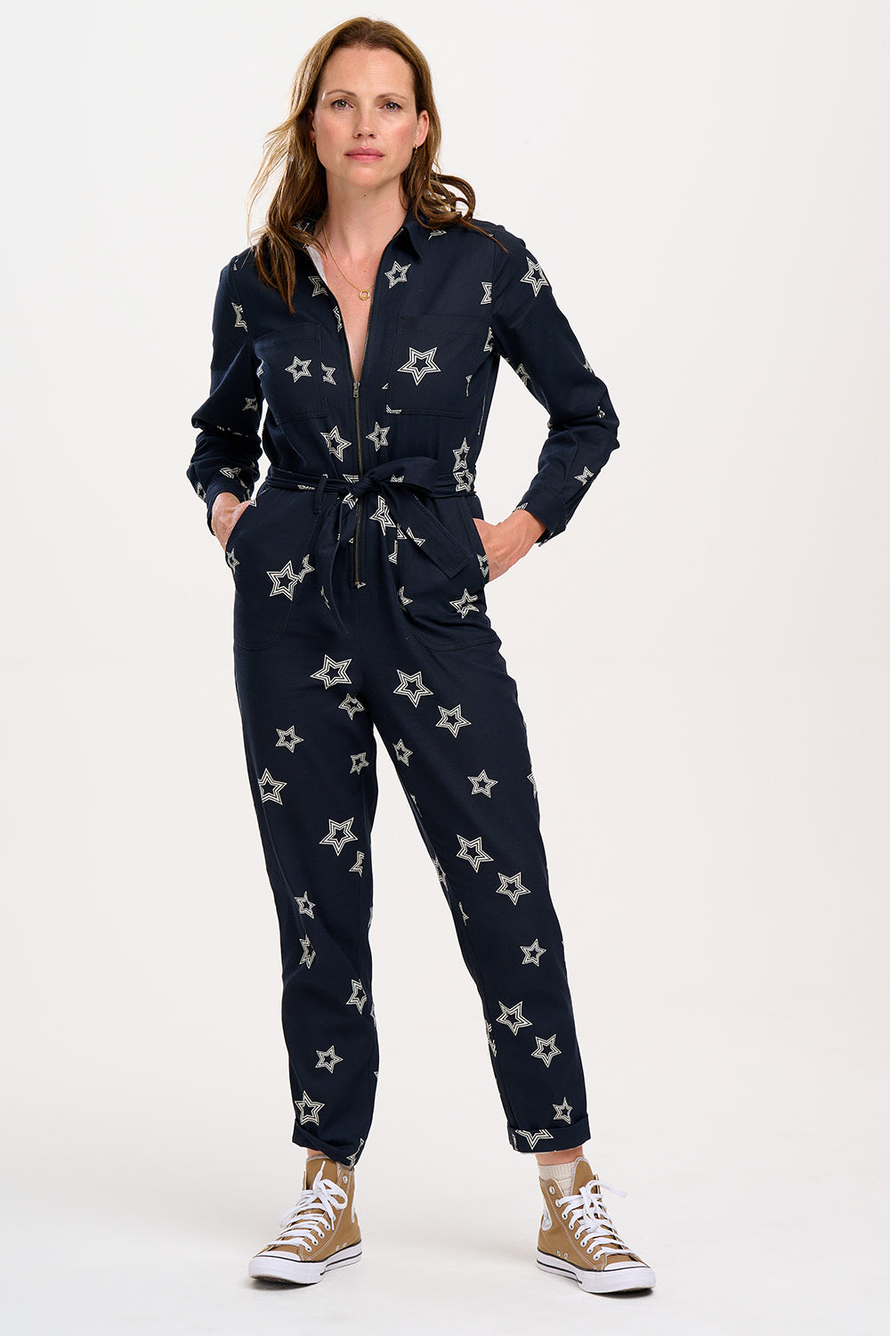 A model wearing a black boilersuit with white triple star patterns on the sleeves and legs, paired with gold sneakers.