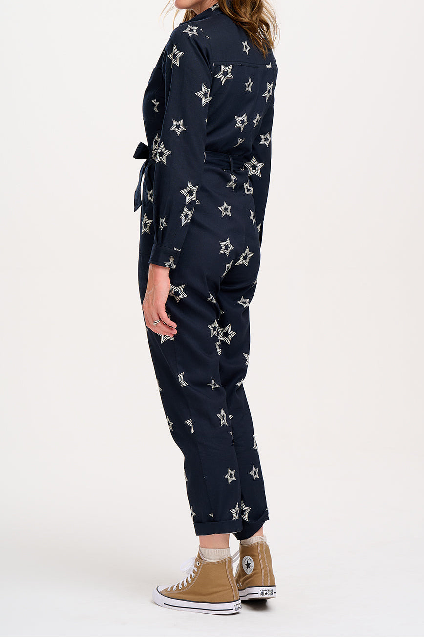 A woman standing in a boilersuit with a black base and white star pattern, featuring a full sleeve shirt upper, exposed front zip, and side pockets. 