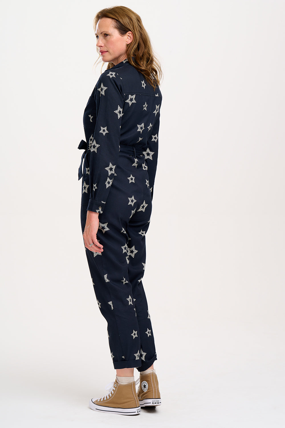 A woman standing in a boilersuit with a black base and white star pattern, featuring a full sleeve shirt upper, exposed front zip, and side pockets. 