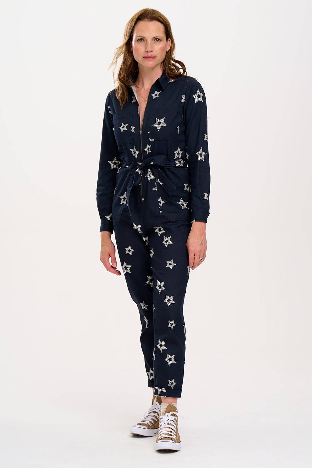 A woman standing in a boilersuit with a black base and white star pattern, featuring a full sleeve shirt upper, exposed front zip, and side pockets. 