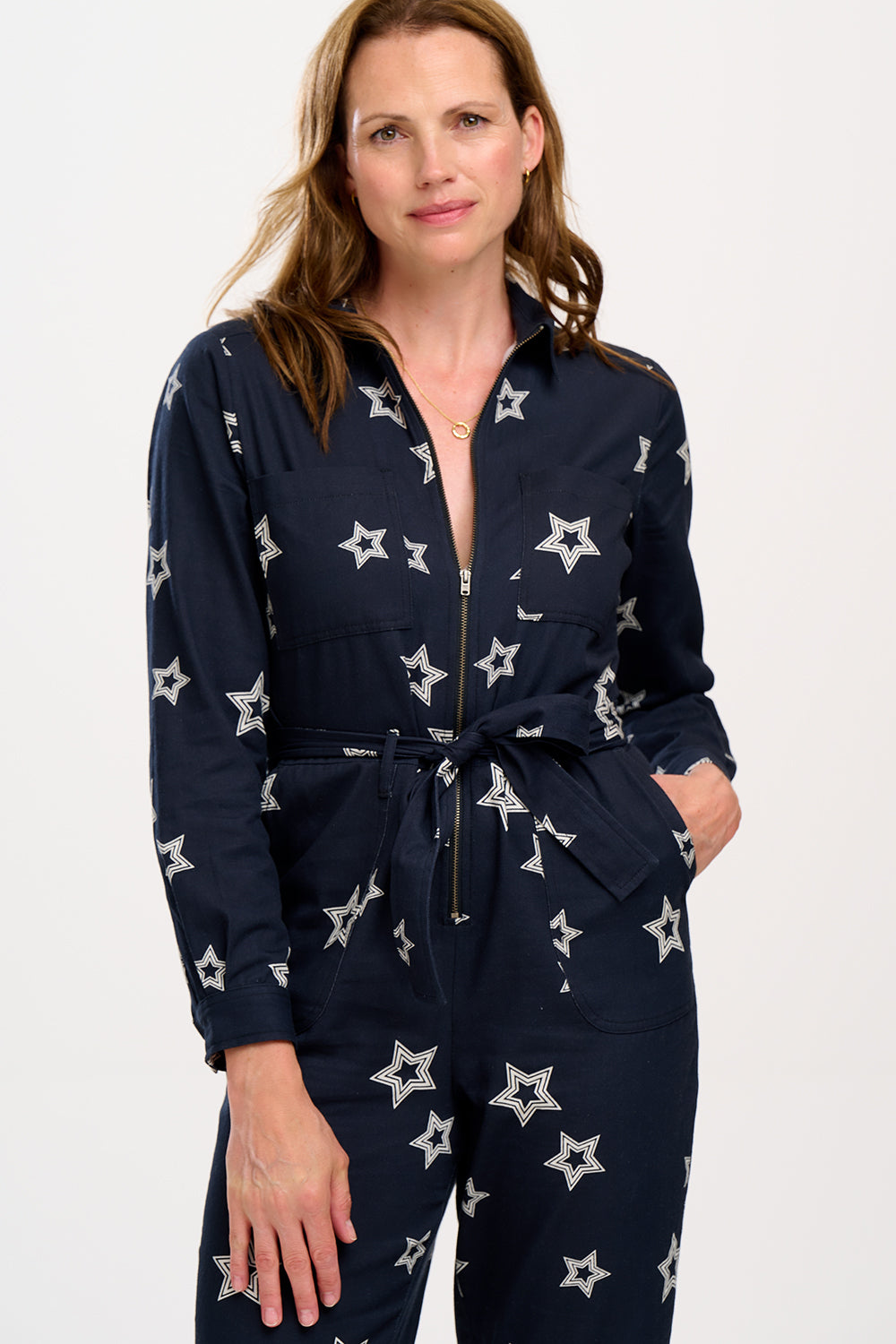 A woman standing in a boilersuit with a black base and white star pattern, featuring a full sleeve shirt upper, exposed front zip, and side pockets. 
