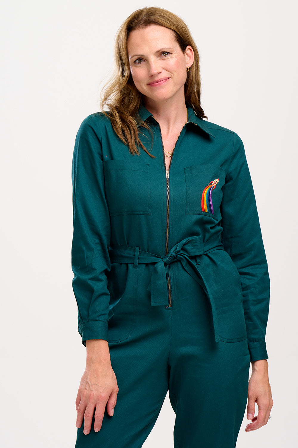 A woman wearing a green boilersuit with a rocket pocket embroidery, paired with white sneakers.