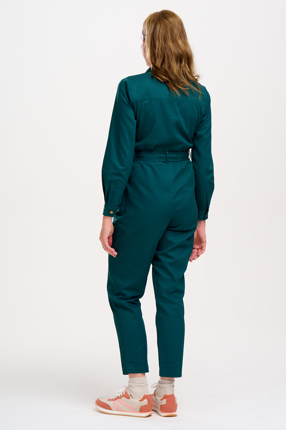 A woman wearing a green boilersuit with a rocket pocket embroidery, paired with white sneakers.