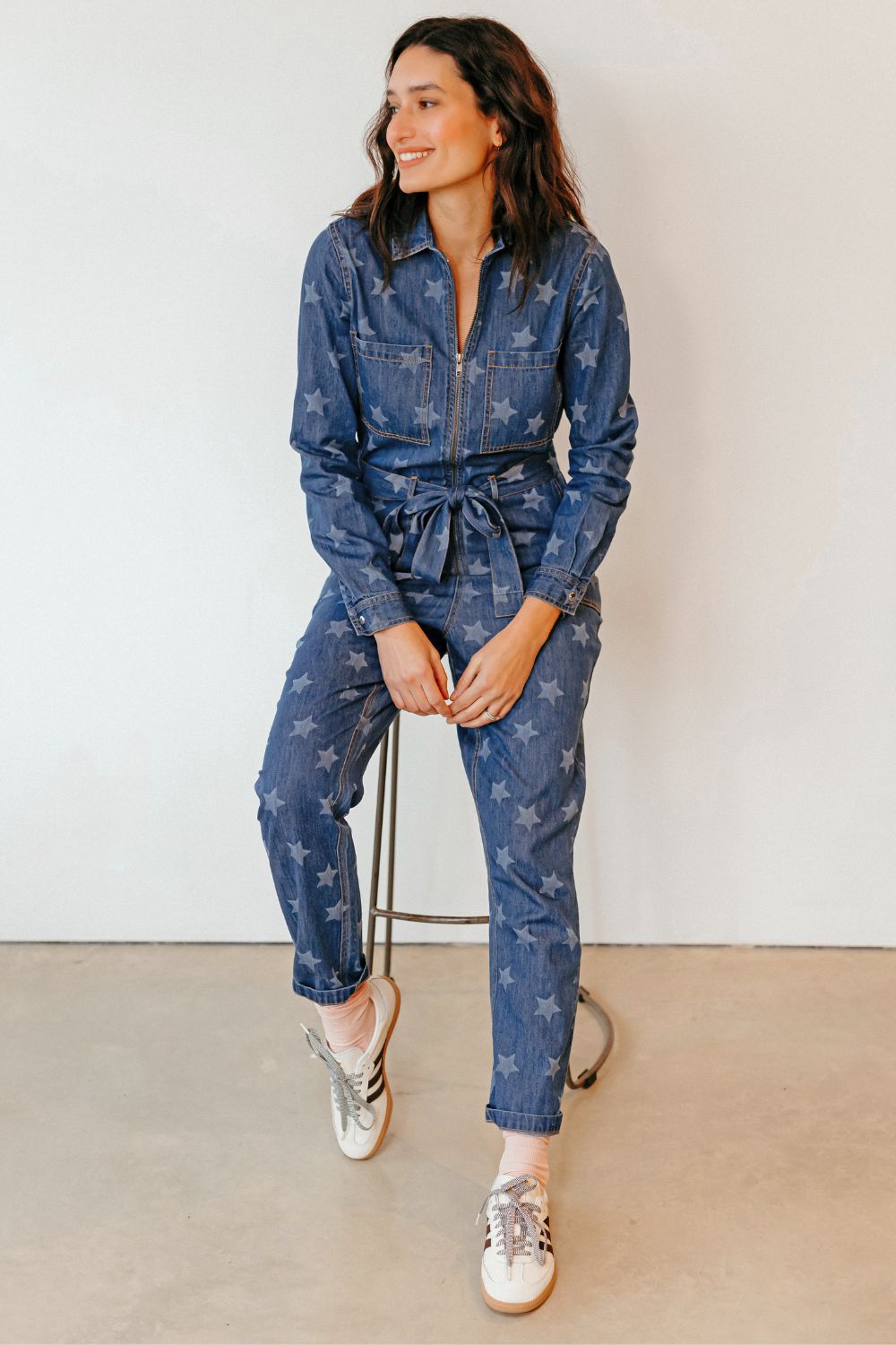 Woman wearing a blue denim jumpsuit with star patterns on a plain background