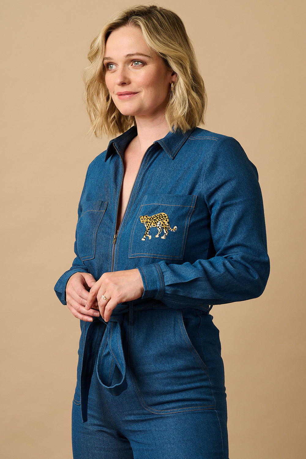 Person wearing a blue jumpsuit on a taupe background