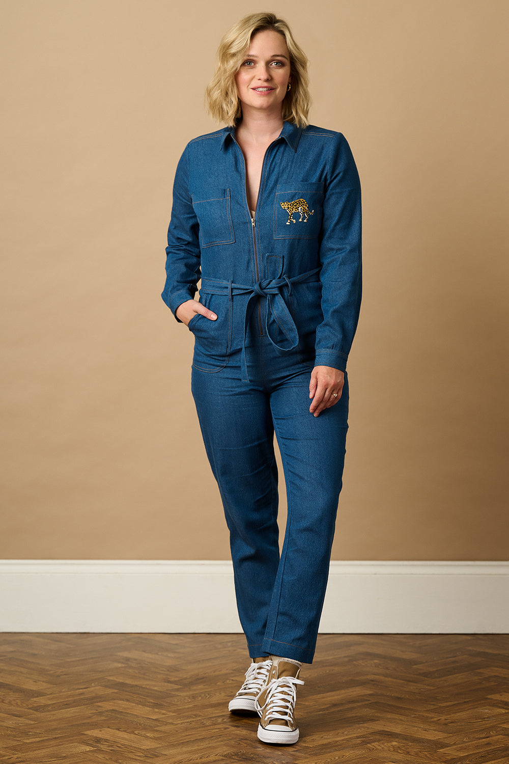 Person wearing a blue jumpsuit on a taupe background