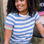 A woman wearing a blue and white striped knit top with rainbow tipping on the cuffs and hem, paired with a denim skirt.