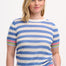A woman wearing a blue and white striped knit top with rainbow tipping on the cuffs and hem, paired with a denim skirt.