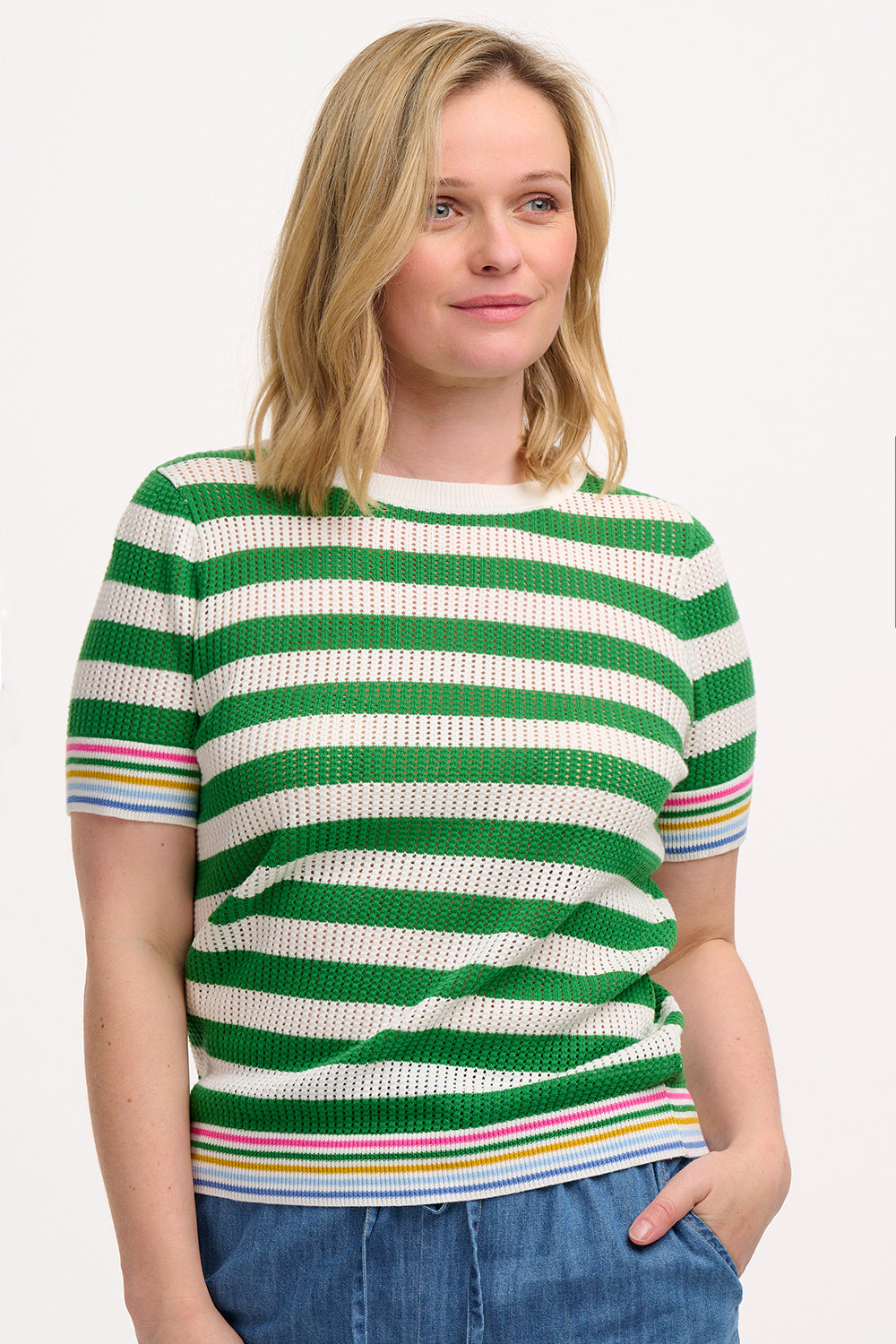 A woman wearing a green and white striped knit top with a crew neck and rainbow tipping on the cuffs and hem.