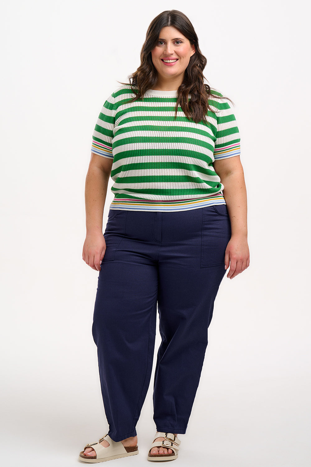 A woman wearing a green and white striped knit top with a crew neck and rainbow tipping on the cuffs and hem.