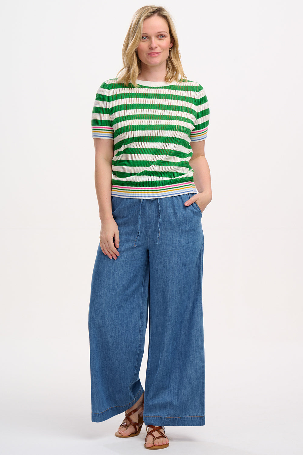 A woman wearing a green and white striped knit top with a crew neck and rainbow tipping on the cuffs and hem.