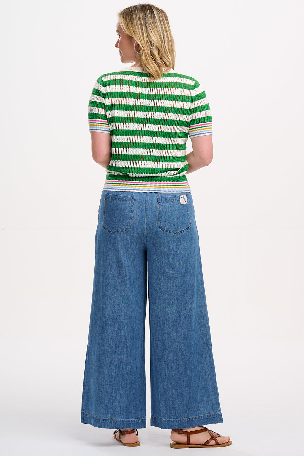 A woman wearing a green and white striped knit top with a crew neck and rainbow tipping on the cuffs and hem.