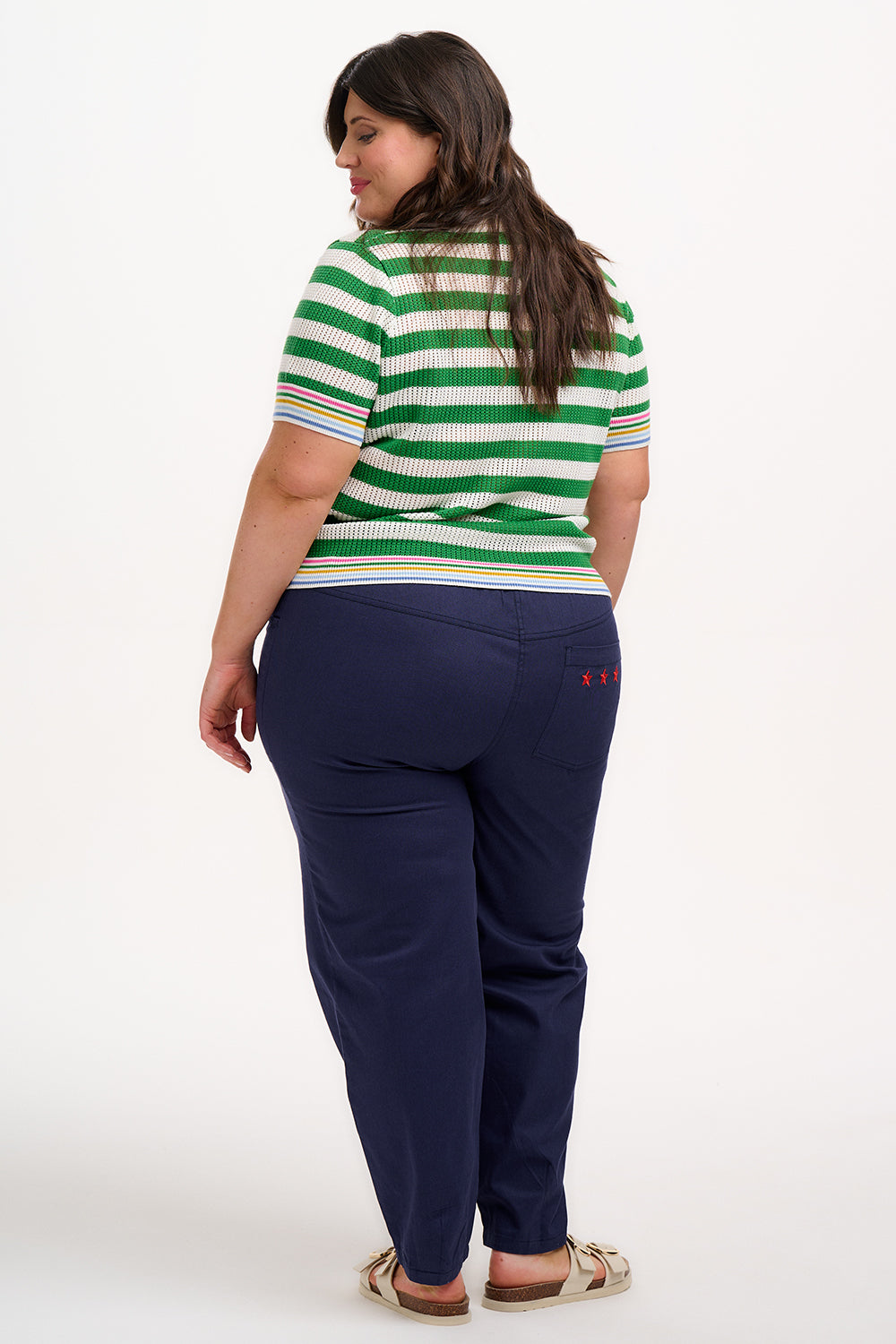 A woman wearing a green and white striped knit top with a crew neck and rainbow tipping on the cuffs and hem.