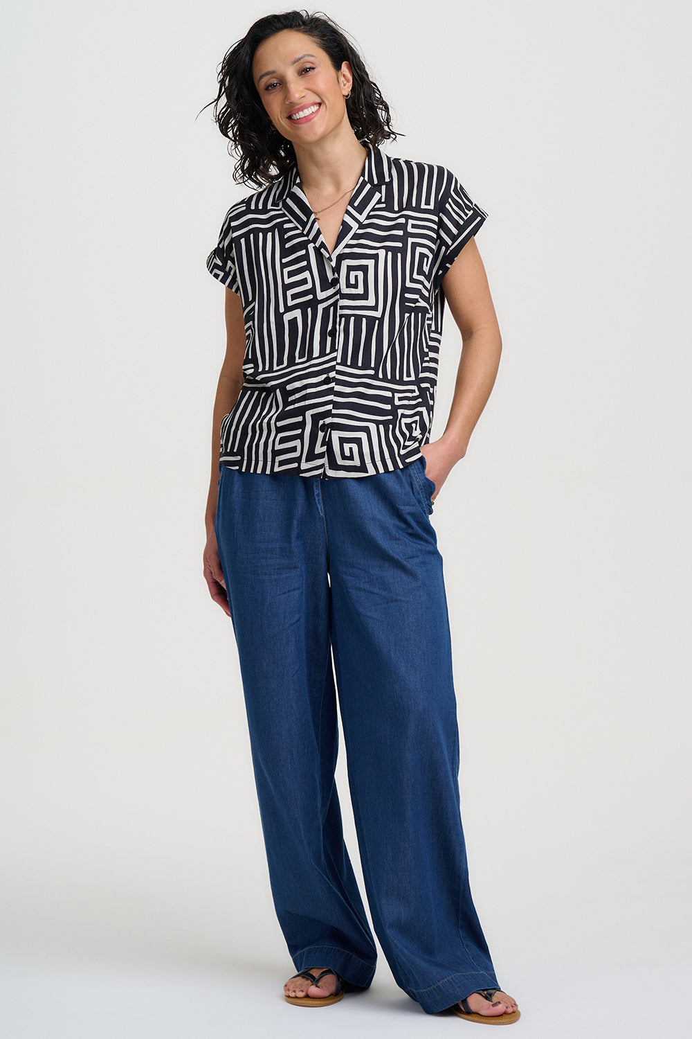 Woman wearing a black and white patterned top and blue pants on a white background