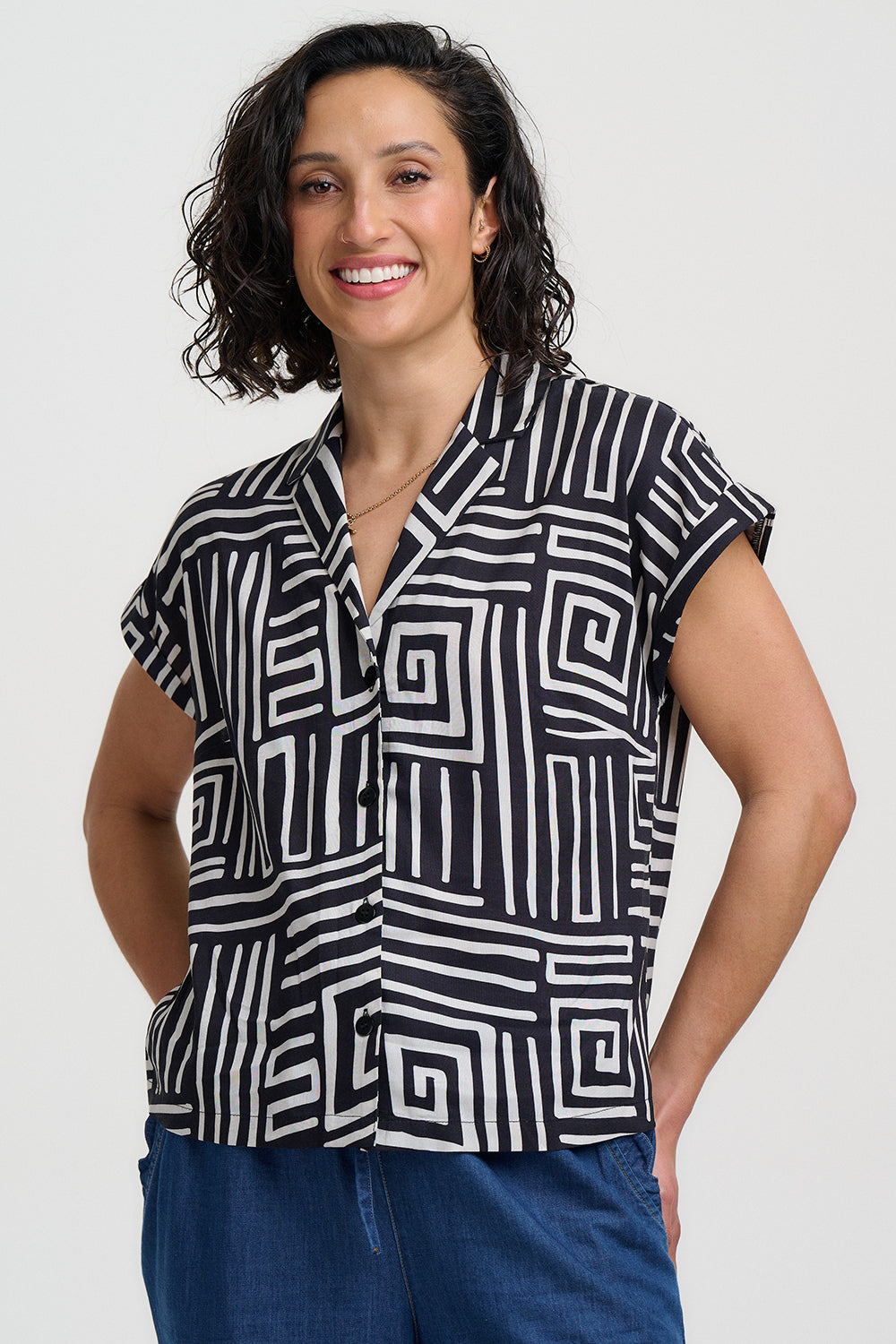 Woman wearing a black and white geometric patterned shirt with blue pants on a white background