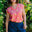 Woman wearing a pink top with banana print and blue shorts standing in a garden.