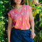Woman wearing a pink top with banana print and blue shorts standing in a garden.