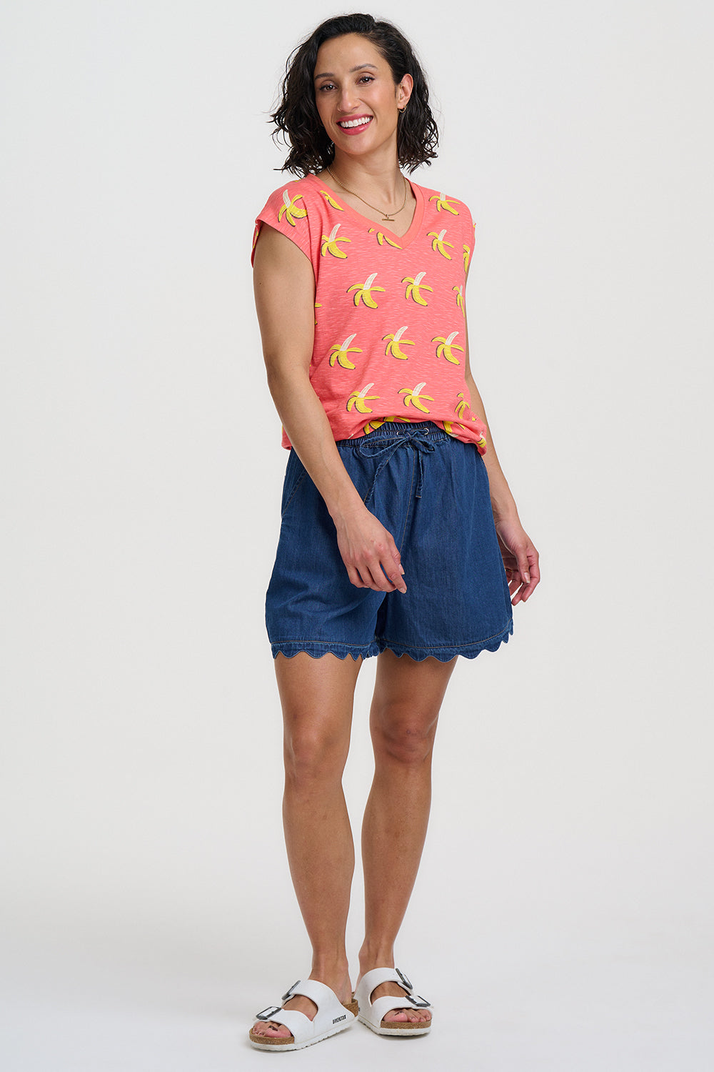 Woman wearing a pink shirt with banana print and blue shorts on a white background