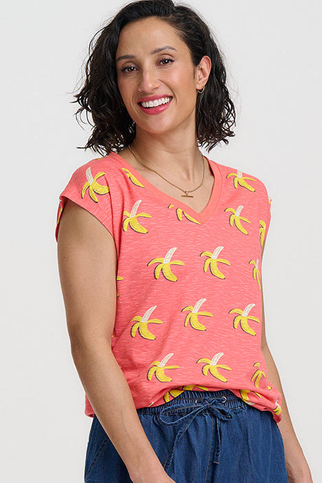 Woman wearing a pink shirt with banana print and blue shorts on a white background