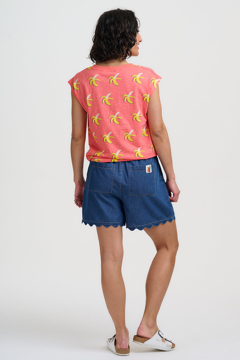 Woman wearing a pink sleeveless top with banana print and blue shorts on a white background