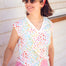 A woman wearing a white V-neck tank t-shirt with a rainbow pebble print, paired with pink pants and accessorized with a red bandana and sunglasses.