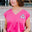 A woman wearing a pink V-neck tank t-shirt with a playful embroidered shark detail, paired with blue denim shorts.