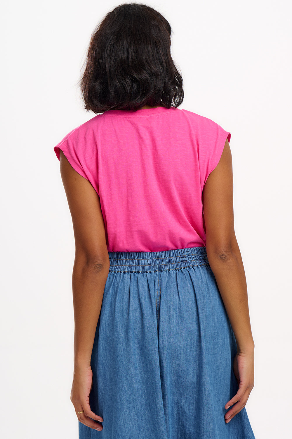 A woman wearing a pink V-neck tank t-shirt with a playful embroidered shark detail