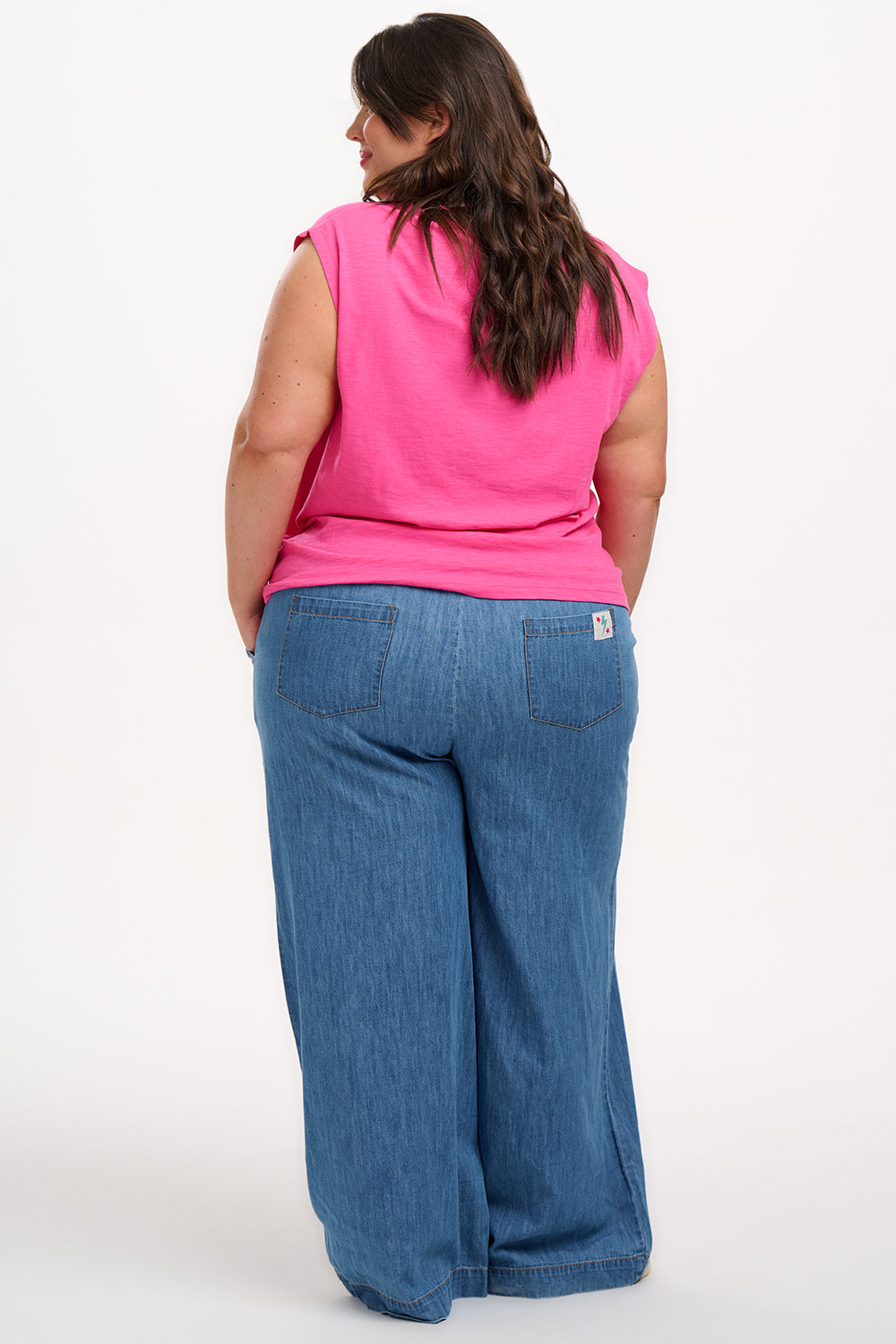 A woman wearing a pink V-neck tank t-shirt with a playful embroidered shark detail