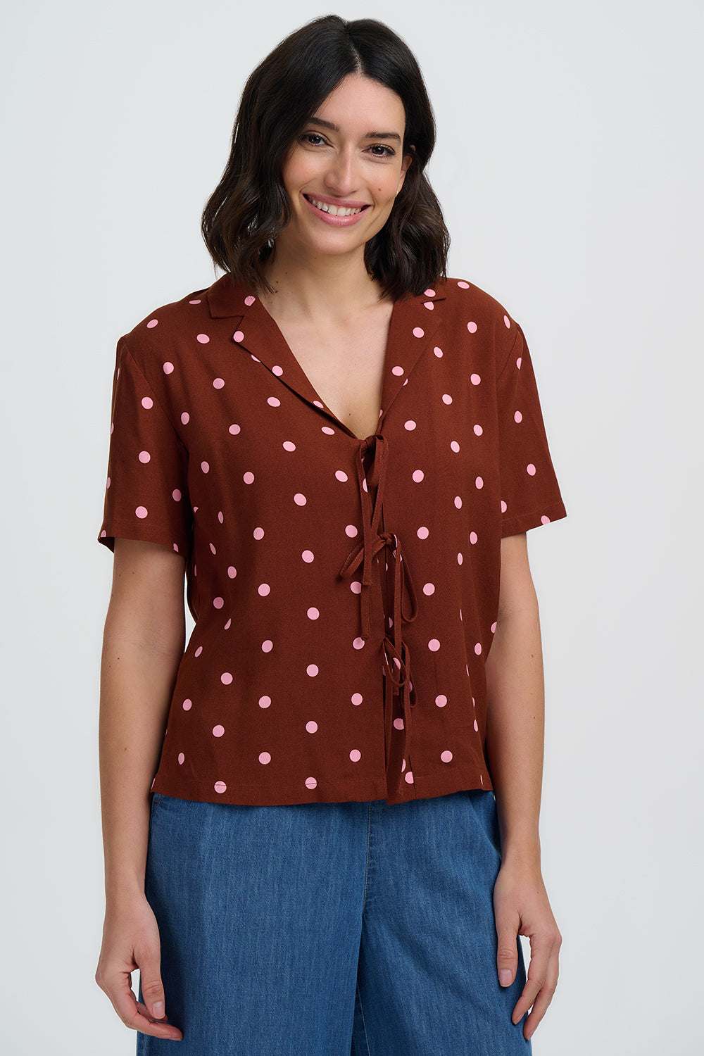 Woman wearing a brown polka dot blouse and blue pants on a white background